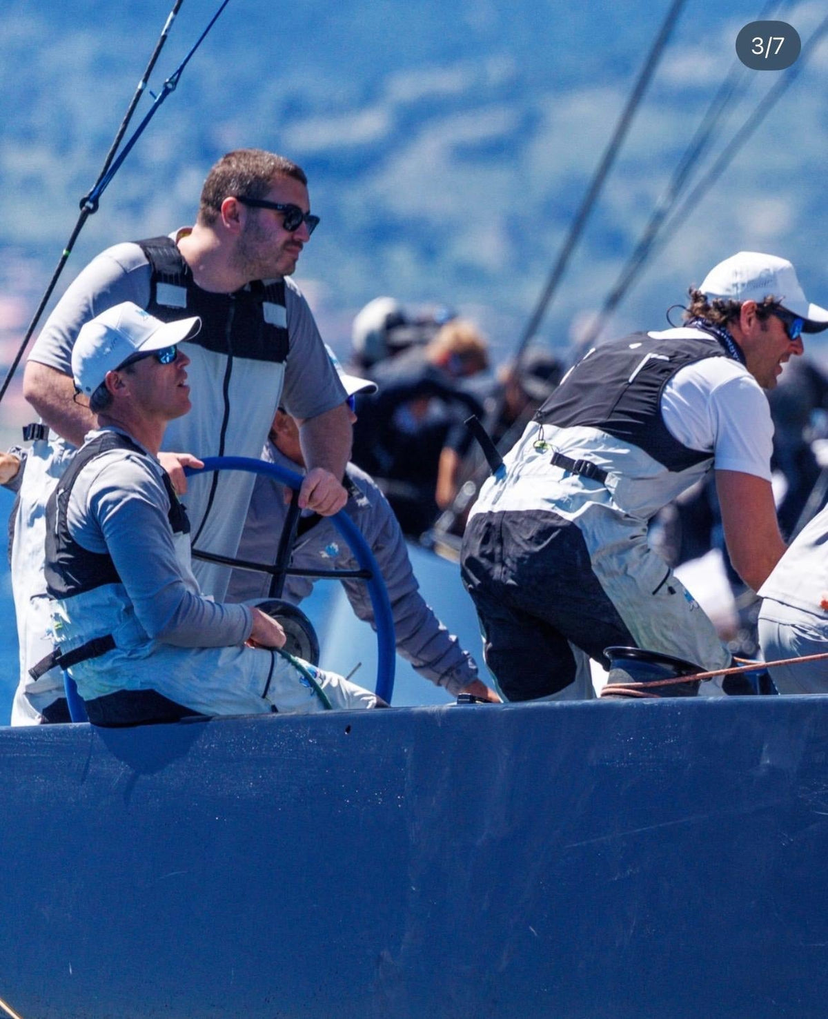 Una tripulación de regata prepara el barco bajo un sol intenso, con reflejos en el agua y ropa técnica náutica.